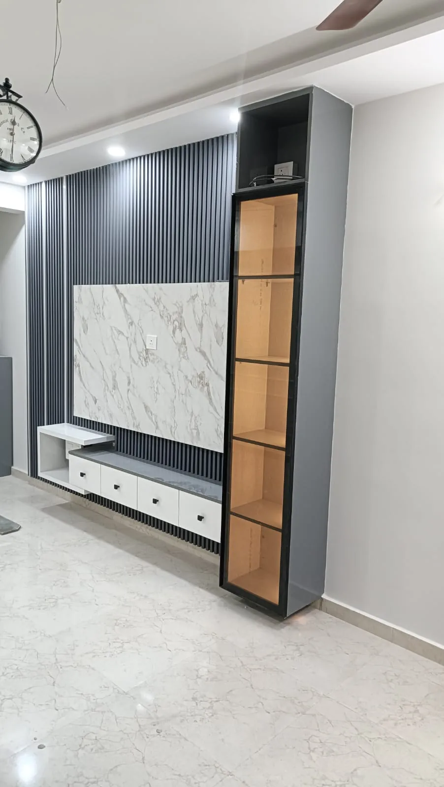 Black fluted media wall with white marble-look TV panel, floating drawers and illuminated side display