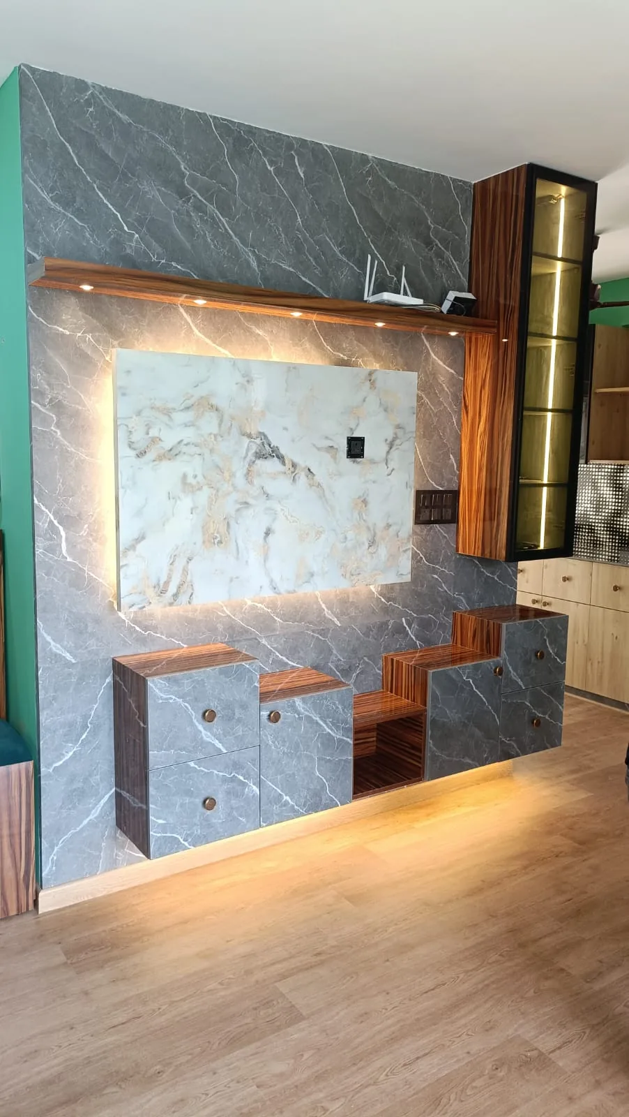 Custom TV feature wall with grey marble-look panels, warm wood shelving and integrated lighting