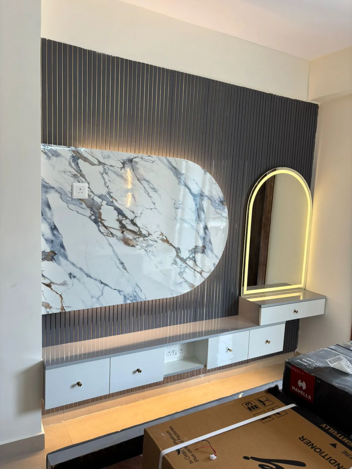 Grey fluted TV feature wall combined with an illuminated arched dressing mirror and white storage