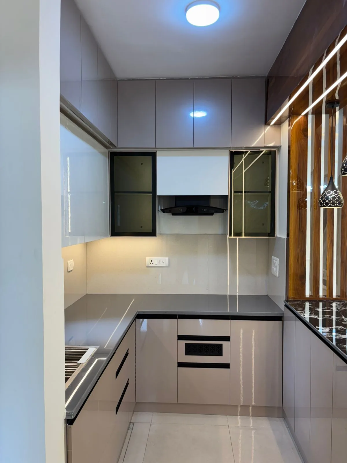 U-shaped taupe modular kitchen with glossy cabinetry, glass upper cabinets and wood partition lighting