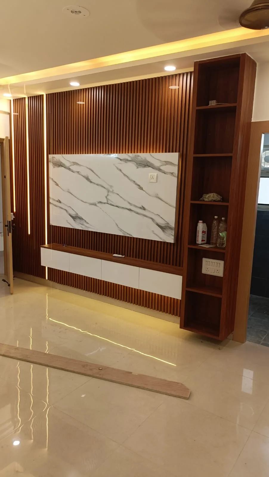 Warm wood slat media wall with marble-look TV panel, side shelving and integrated LED lighting